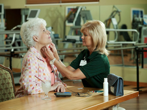 A healthcare professional assists an elderly patient in a clinical setting.