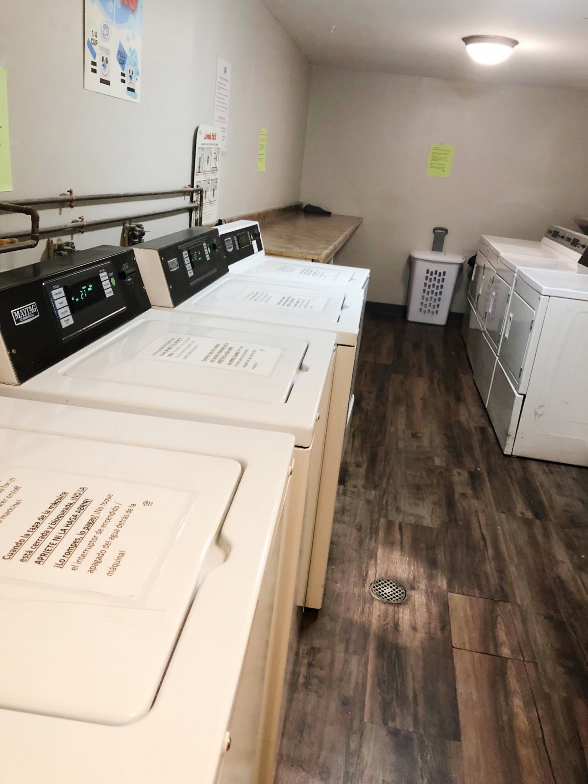 A laundry room with several washing machines and dryers on a wooden floor.