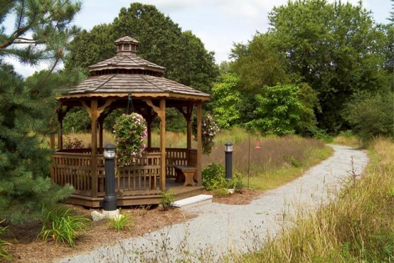 A wooden gazebo surrounded by lush greenery and a gravel pathway.