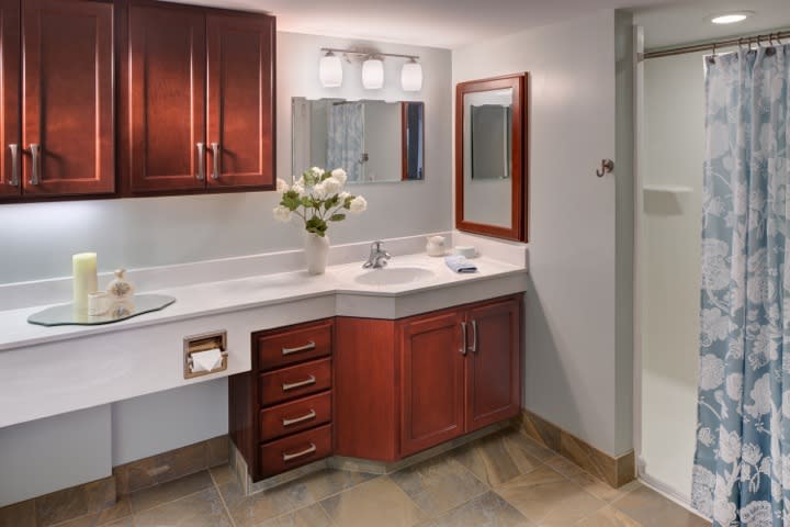 A modern bathroom vanity with a wooden cabinet, decorative flowers, and bright lighting.