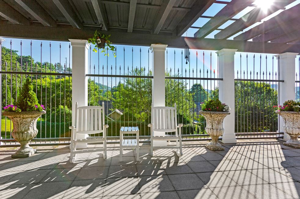 A sunny patio with white rocking chairs under a pergola, offering a serene garden view.