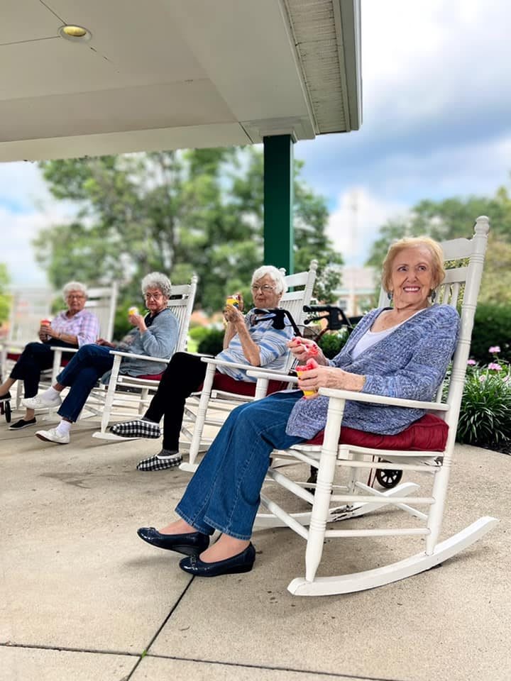 A group of elderly women relaxing on rocking chairs on a porch.