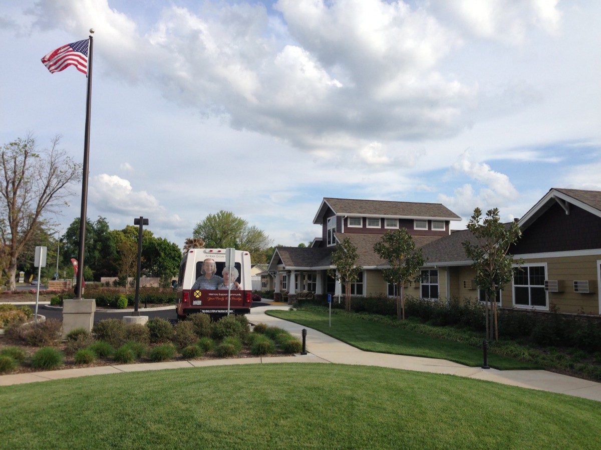 A scenic view of a building with a flagpole, surrounded by a well-maintained lawn and trees under a cloudy sky.