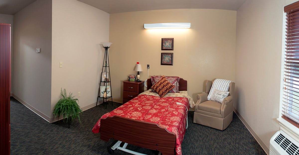 A cozy bedroom with a single bed, lamp, and comfortable chair.
