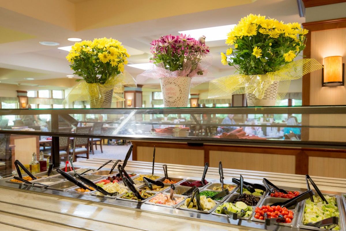 A vibrant buffet salad bar with an array of fresh vegetables and decorative flower arrangements above.