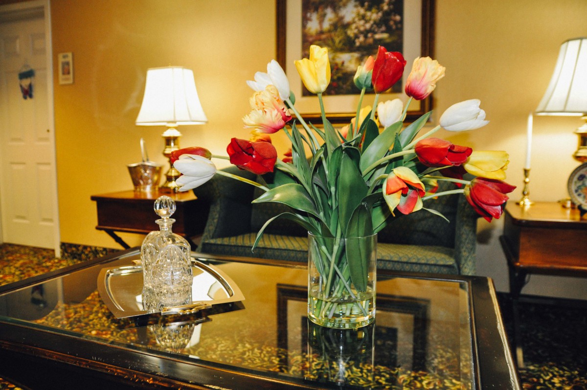 A beautifully arranged bouquet of tulips in a vase sits on a polished table next to an ornate glass bottle, with a softly glowing lamp in the background.