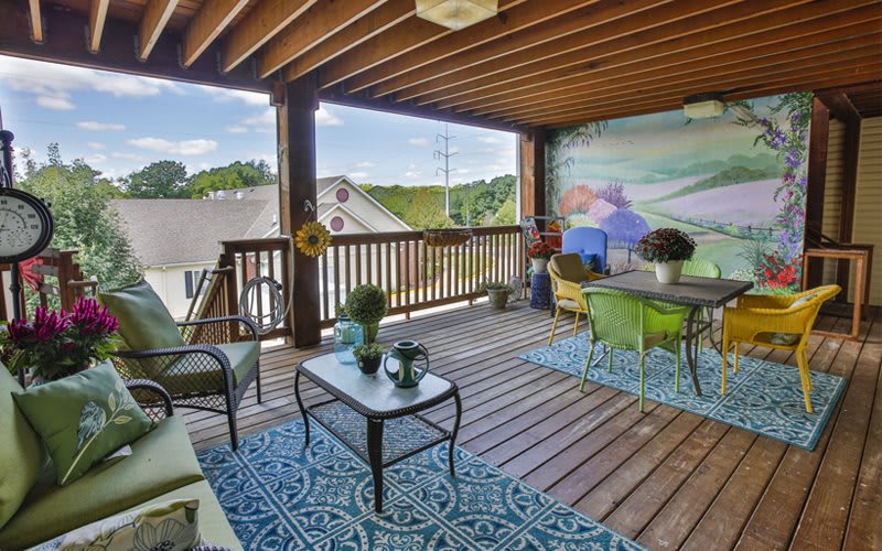 A cozy outdoor patio with wooden flooring, stylish furniture, and decorative plants under a covered roof.