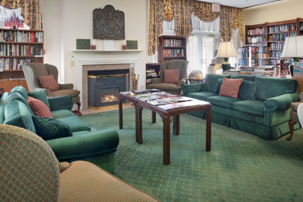 A cozy living room featuring green furniture, a fireplace, and a well-stocked bookshelf.