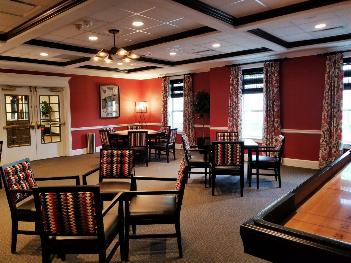 A cozy dining room with multiple tables and chairs, warm lighting, and red walls with large windows.