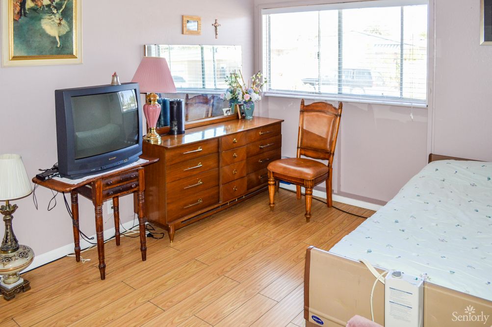 A cozy bedroom with vintage furniture, including a TV, dresser, and chair.