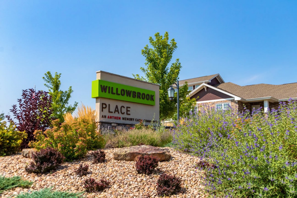 A landscaped area featuring a sign for Willowbrook Place with a building in the background.