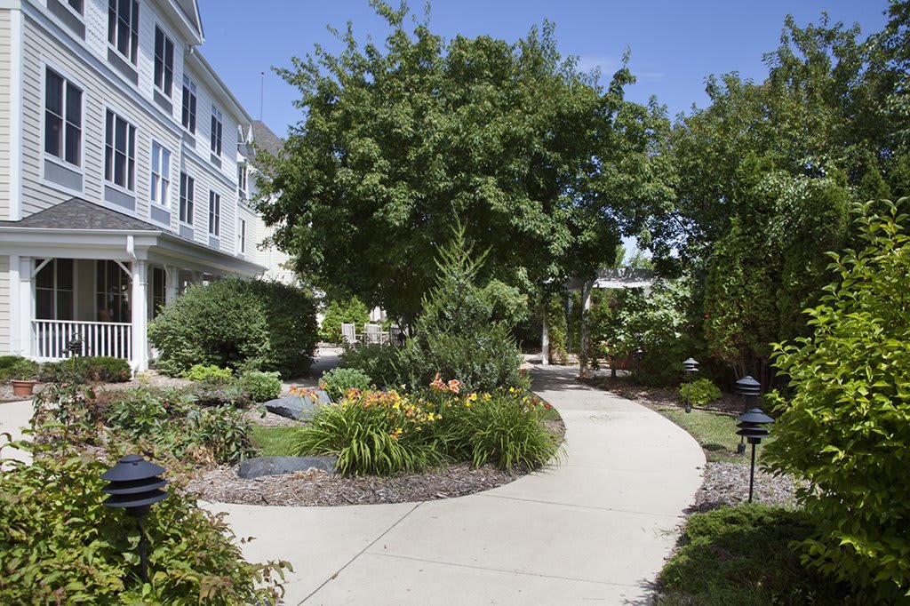 A scenic garden pathway surrounded by lush greenery and a building on a sunny day.