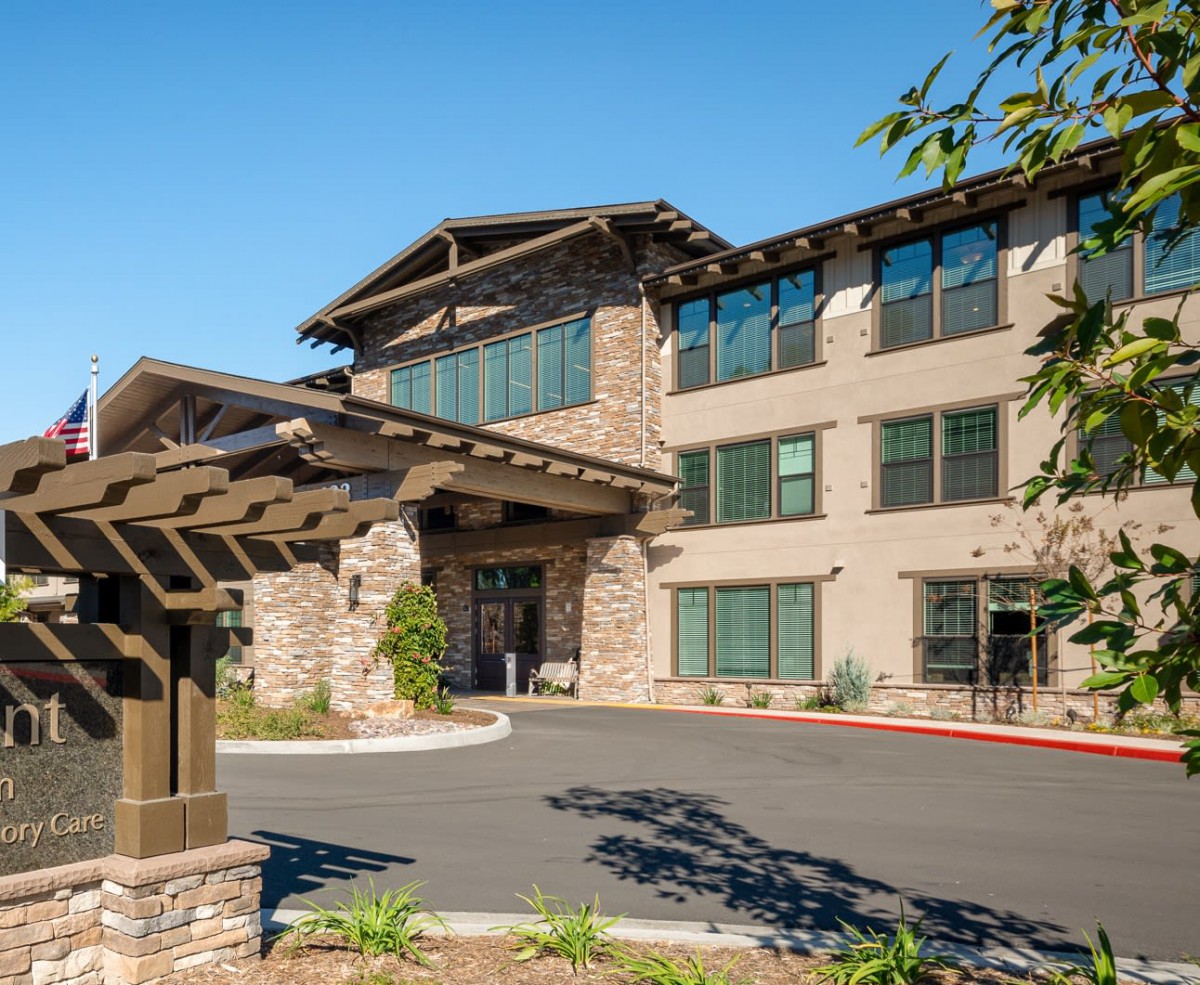 A modern residential building with a landscaped entrance under a clear blue sky.