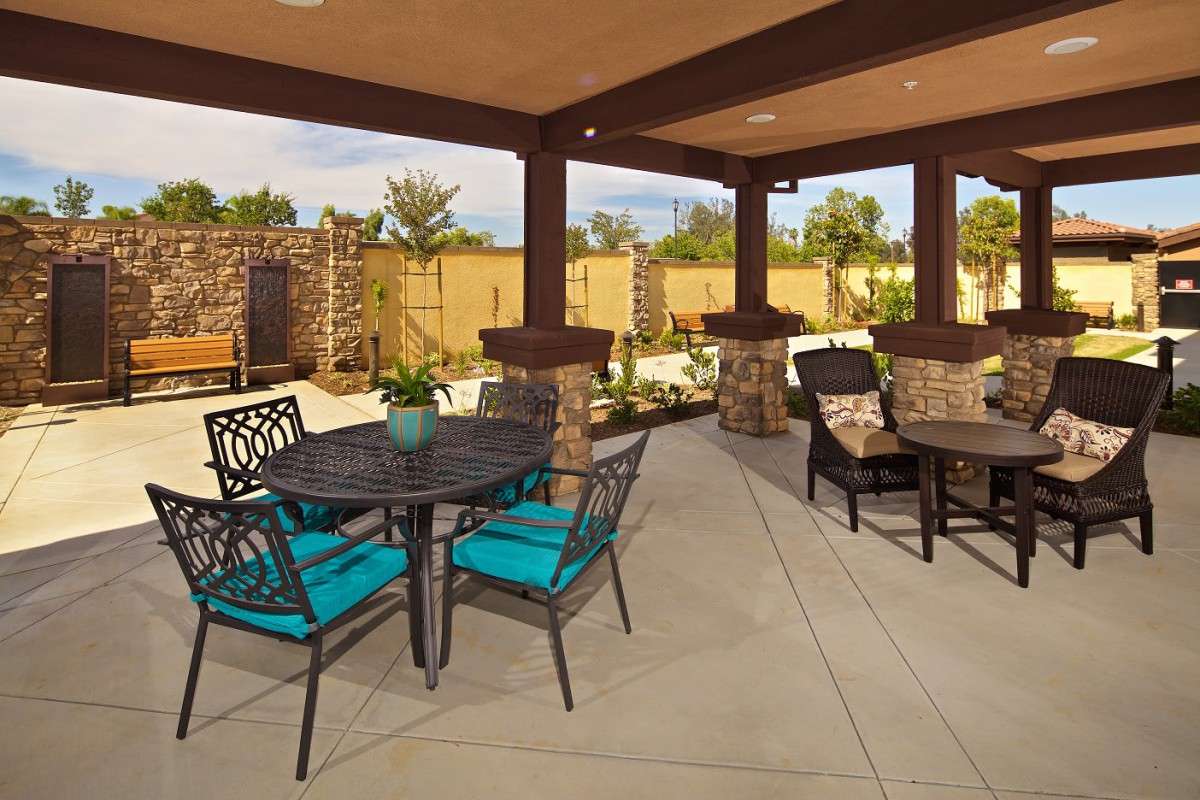 A spacious outdoor patio with tables and chairs, under a covered area, surrounded by landscaped gardens.