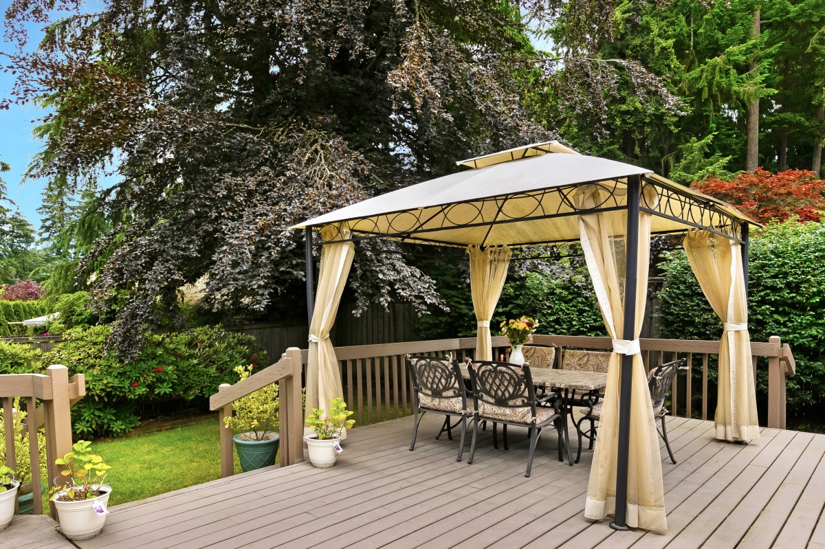 A cozy outdoor gazebo on a wooden deck surrounded by lush greenery.