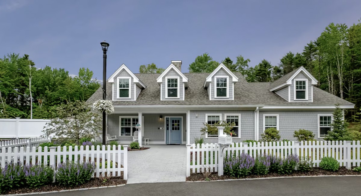 A charming gray house with a white picket fence and landscaped garden.