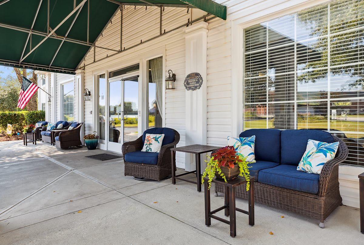 A cozy outdoor patio area with wicker furniture and potted plants under a green awning.