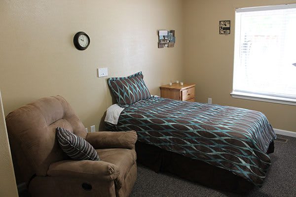 A cozy bedroom with a single bed, armchair, and window letting in natural light.
