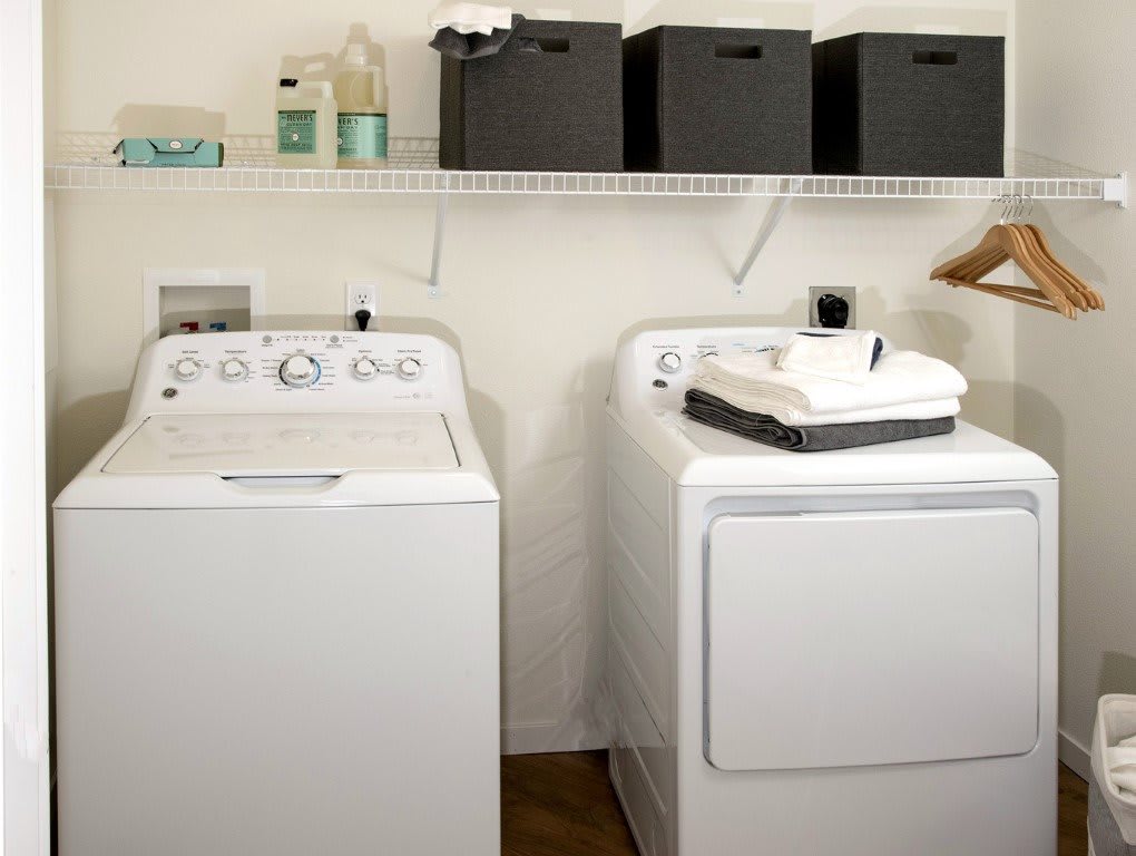 A neatly organized laundry room featuring a washing machine and dryer with storage shelves above.