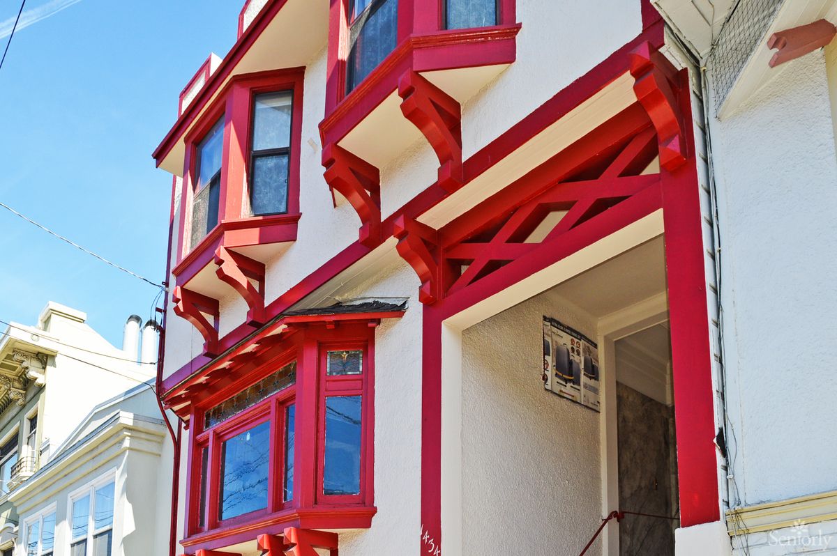 A residential building featuring distinctive red accents on bay windows and structural elements.