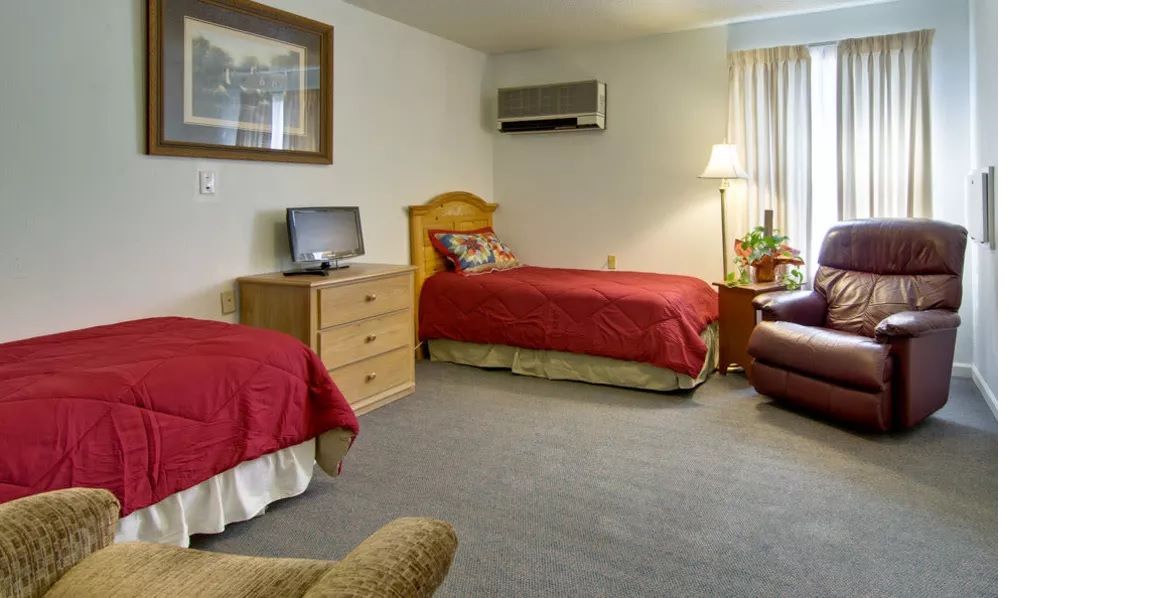 A cozy bedroom with a single bed, television, armchair, and air conditioning unit.
