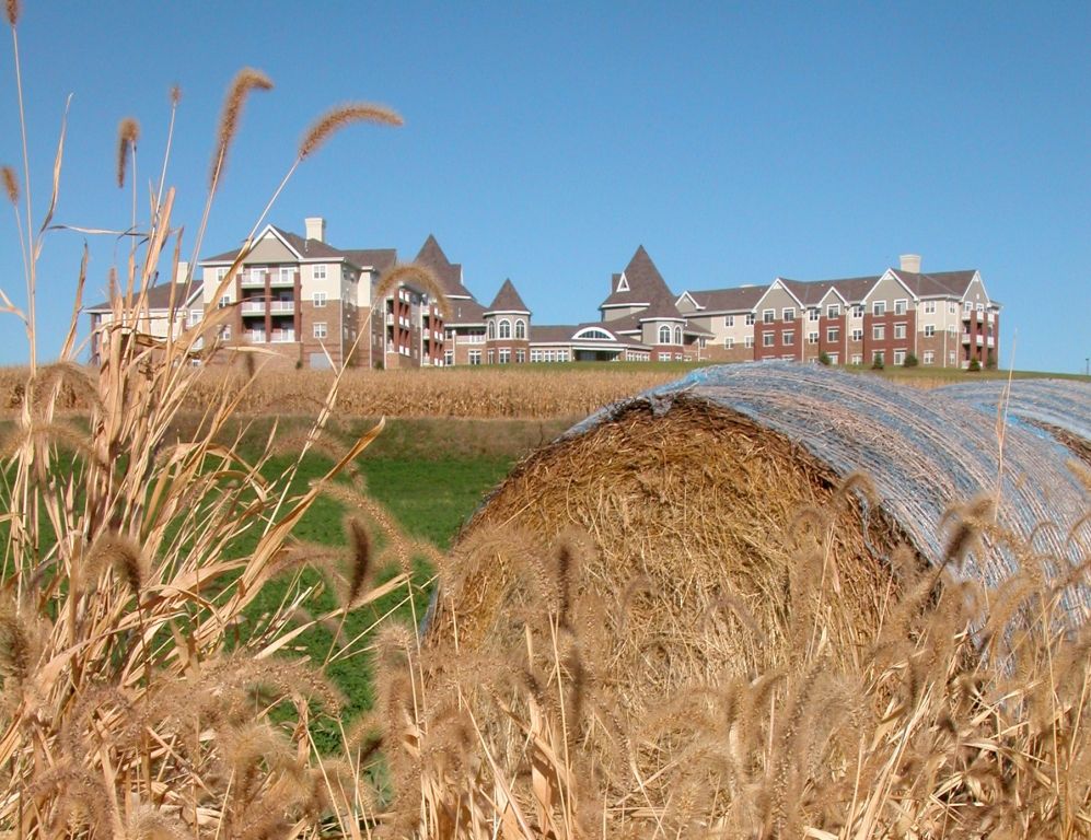 A rural scene featuring a hay bale in the foreground with residential buildings in the background.
