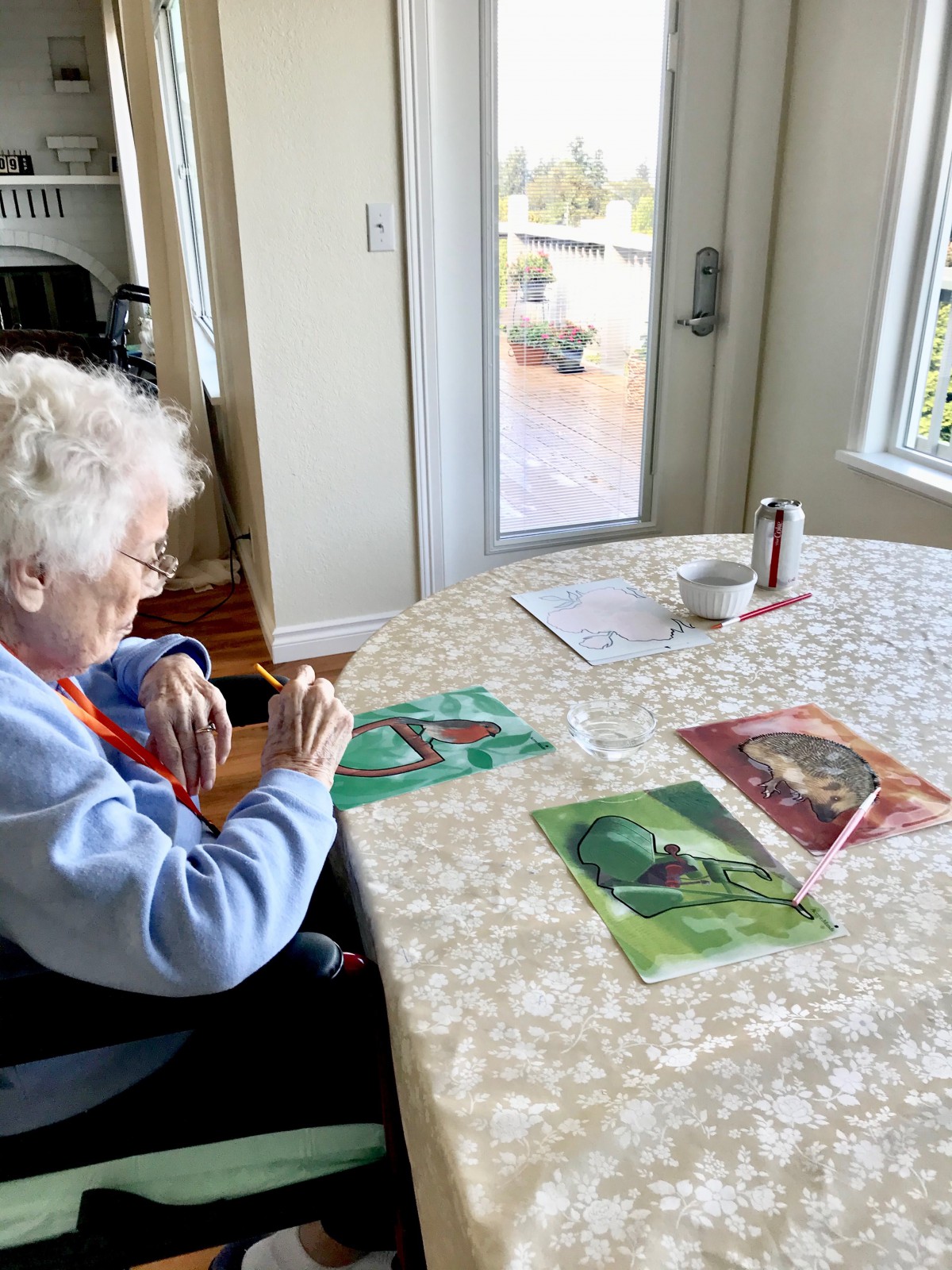 An elderly woman sitting at a table engaged in crafting activities with puzzle pieces.