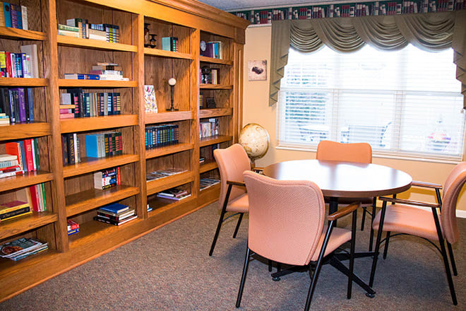 A cozy library corner with bookshelves, a round table surrounded by chairs, and a globe by the window.