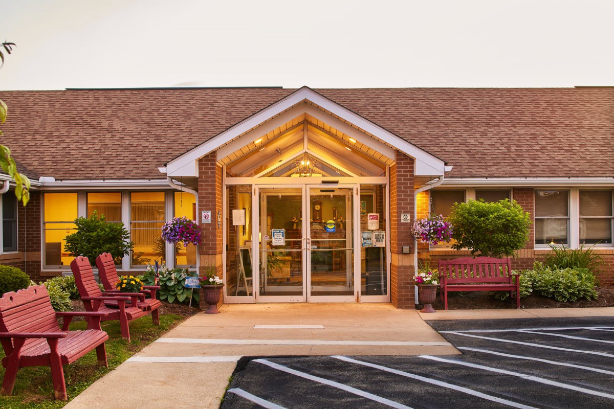 A welcoming entrance to a brick building, adorned with flowers and benches.