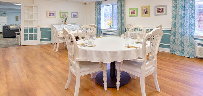 A bright dining room with white round tables and chairs, featuring elegant decor and wooden floors.