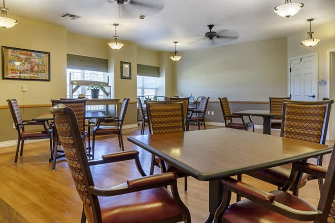 A dining area with several tables and chairs, ceiling fans, and windows providing natural light.