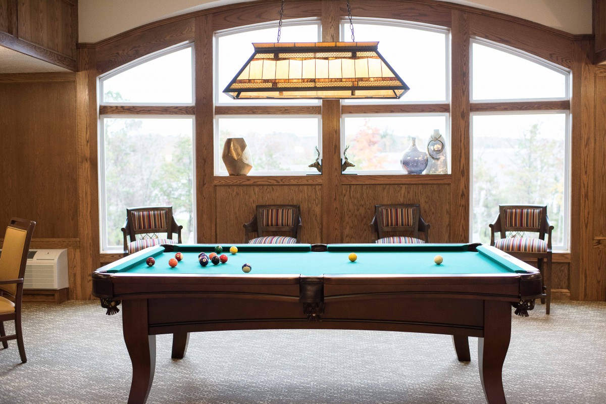 A cozy game room featuring a billiard table with stylish lighting and comfortable seating by large windows.