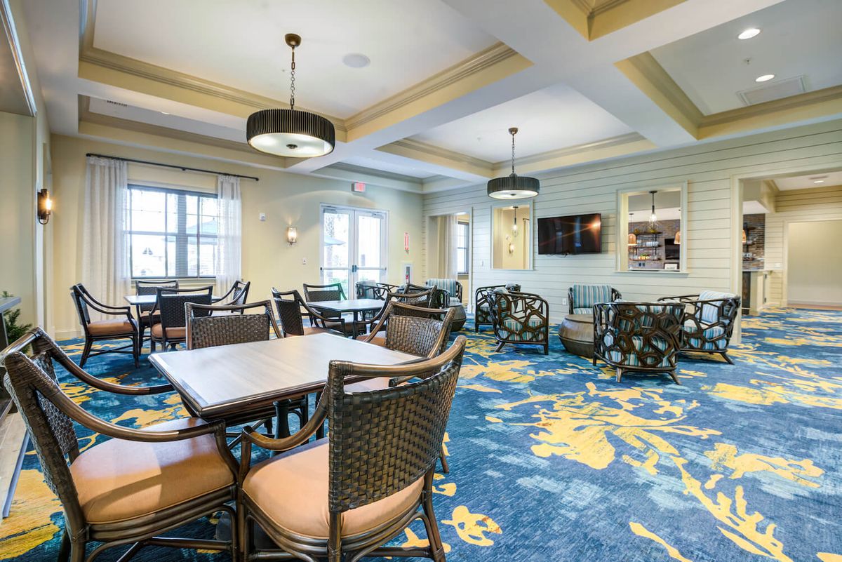 A well-furnished dining room with contemporary decor, featuring tables and chairs on a vibrant blue carpet, illuminated by ceiling lights.