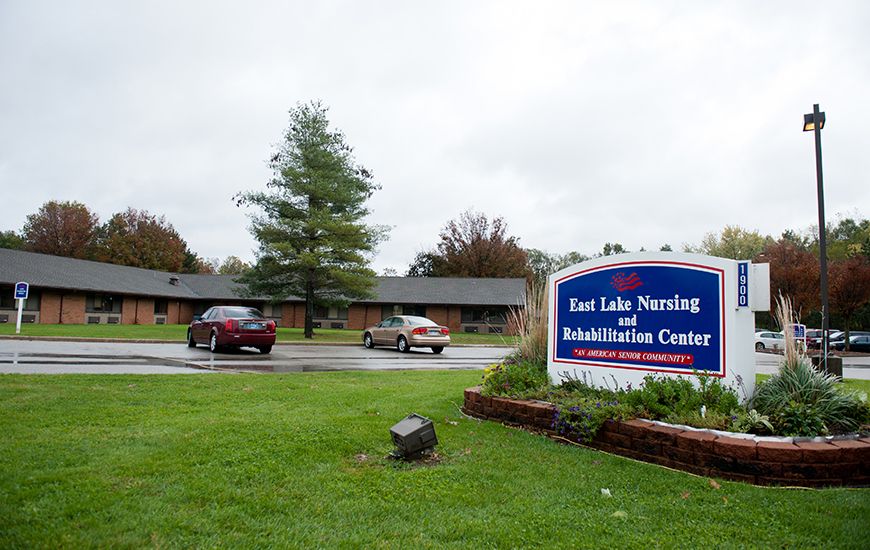 Exterior view of East Lake Nursing and Rehabilitation Center with a parking area and garden.