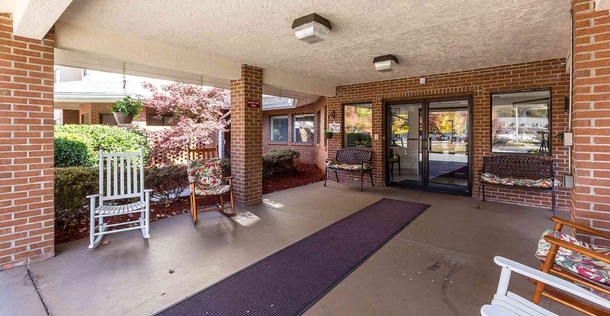 A covered building entrance with a bench, decorative plants, and glass doors.