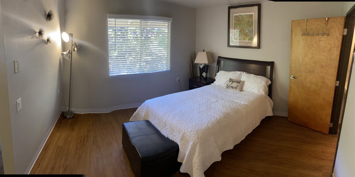 A cozy bedroom with a neatly made bed, bedside lamp, and a window allowing natural light to brighten the room.