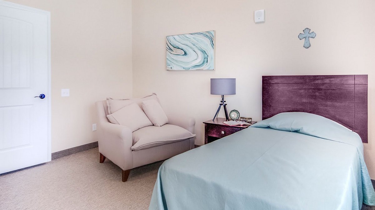 A cozy bedroom corner featuring a plush chair, a bedside table with a lamp, and serene wall art.