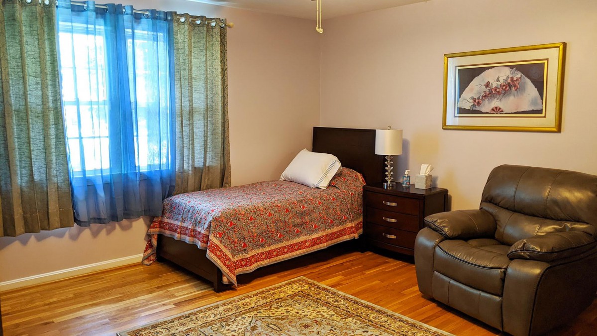 A cozy bedroom with a single bed, nightstand, and a lamp on a hardwood floor.