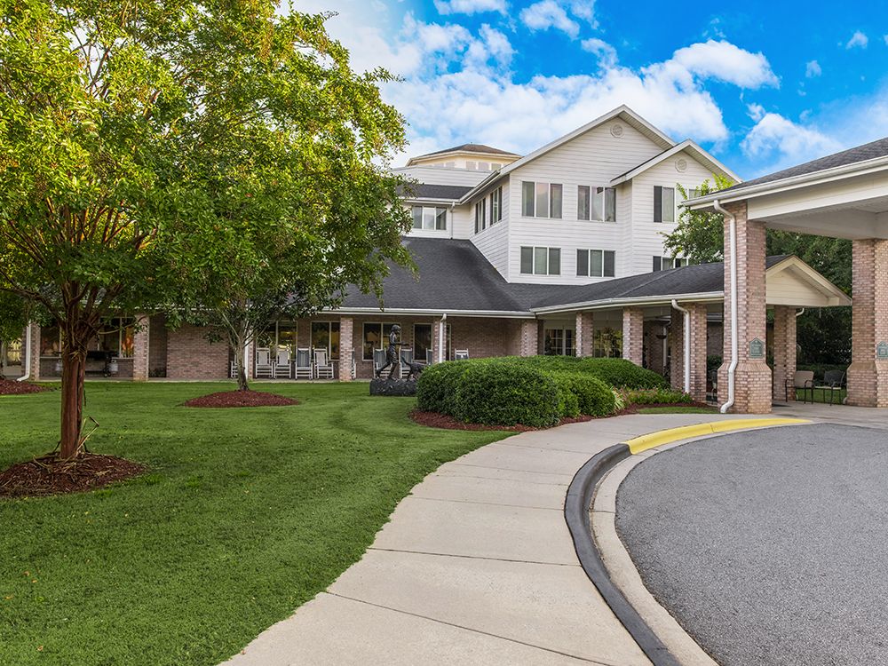 A white residential building with a landscaped garden and a curving pathway under a partly cloudy sky.