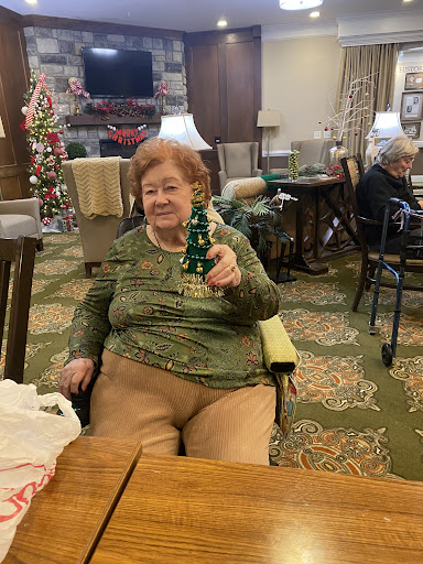 An elderly woman enjoying a festive moment while holding a small green Christmas tree decoration.