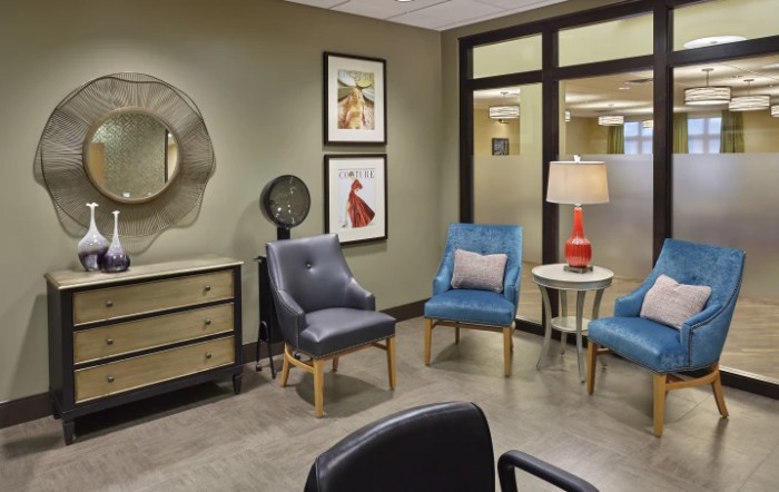 A modern waiting room with stylish chairs, a small table with a lamp, and decorative wall art.