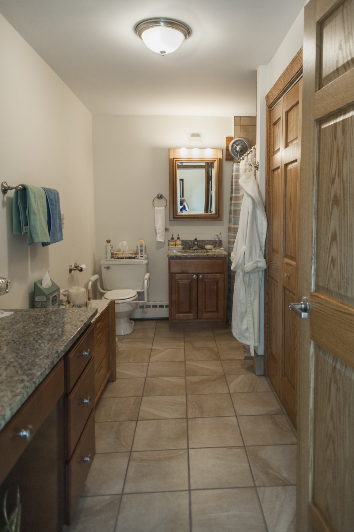 A well-organized bathroom with a wooden vanity, tiled floor, and hanging robes.