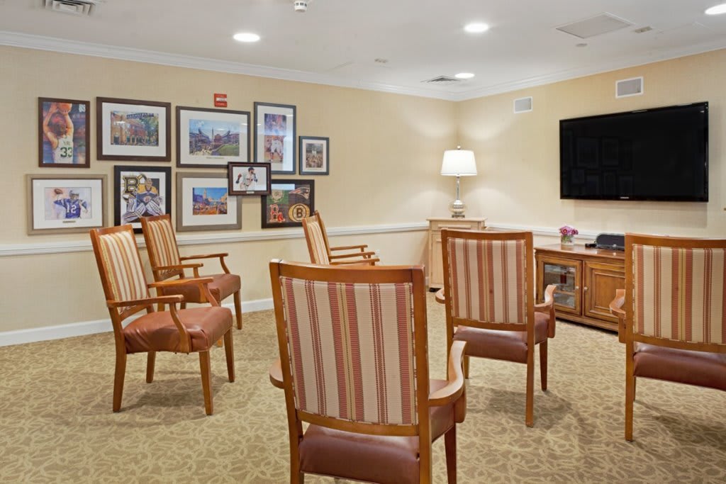 A cozy living room setup with chairs arranged around a television, surrounded by framed photos on the wall.