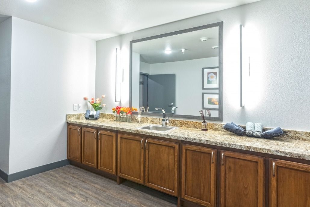 A spacious bathroom featuring a large mirror, granite countertop, and wooden cabinets with modern lighting.