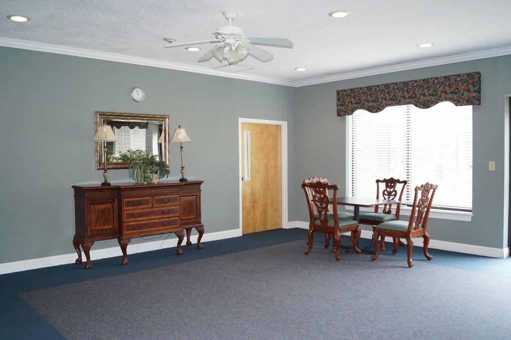 A classic dining room with a sideboard, table, and chairs, adorned by a mirror and window with curtains.