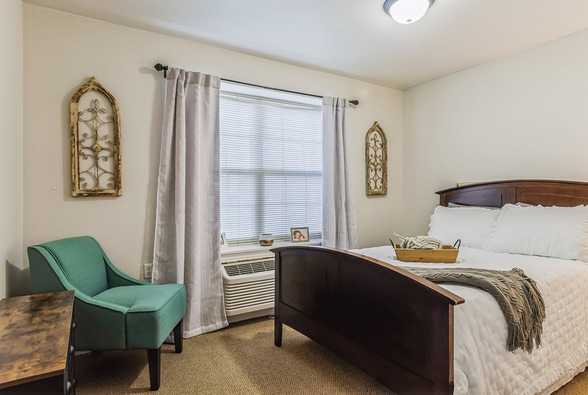 A cozy bedroom with a neatly made bed, teal armchair, and decorative wall art.