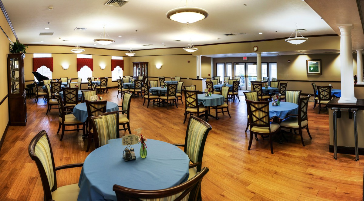 A spacious dining room with neatly arranged tables and chairs, featuring a warm wooden floor and elegant lighting.