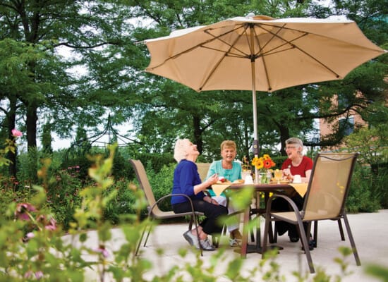 A group of friends enjoying a conversation at a patio table under a large umbrella.