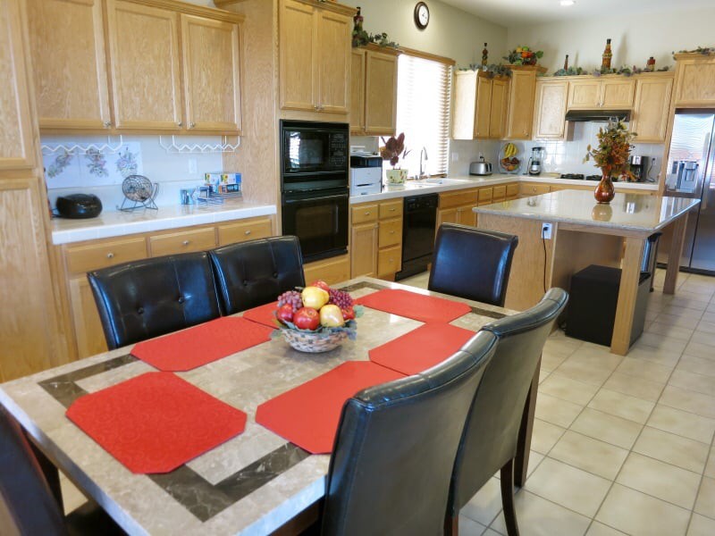A spacious kitchen and dining area featuring wooden cabinets, a central dining table with red placemats, and modern appliances.