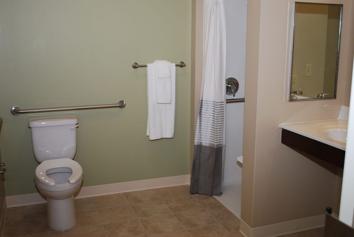 A clean bathroom with a toilet, shower, and towel on a green wall.
